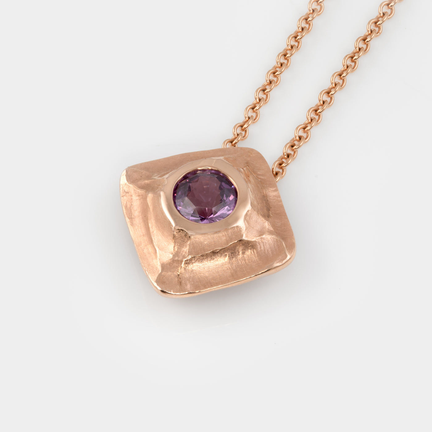 Textured rose gold necklace with purple sapphire on a white background
