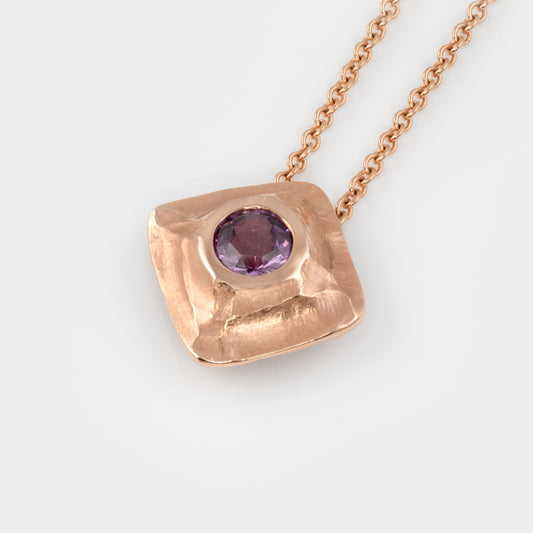 Textured rose gold necklace with purple sapphire on a white background