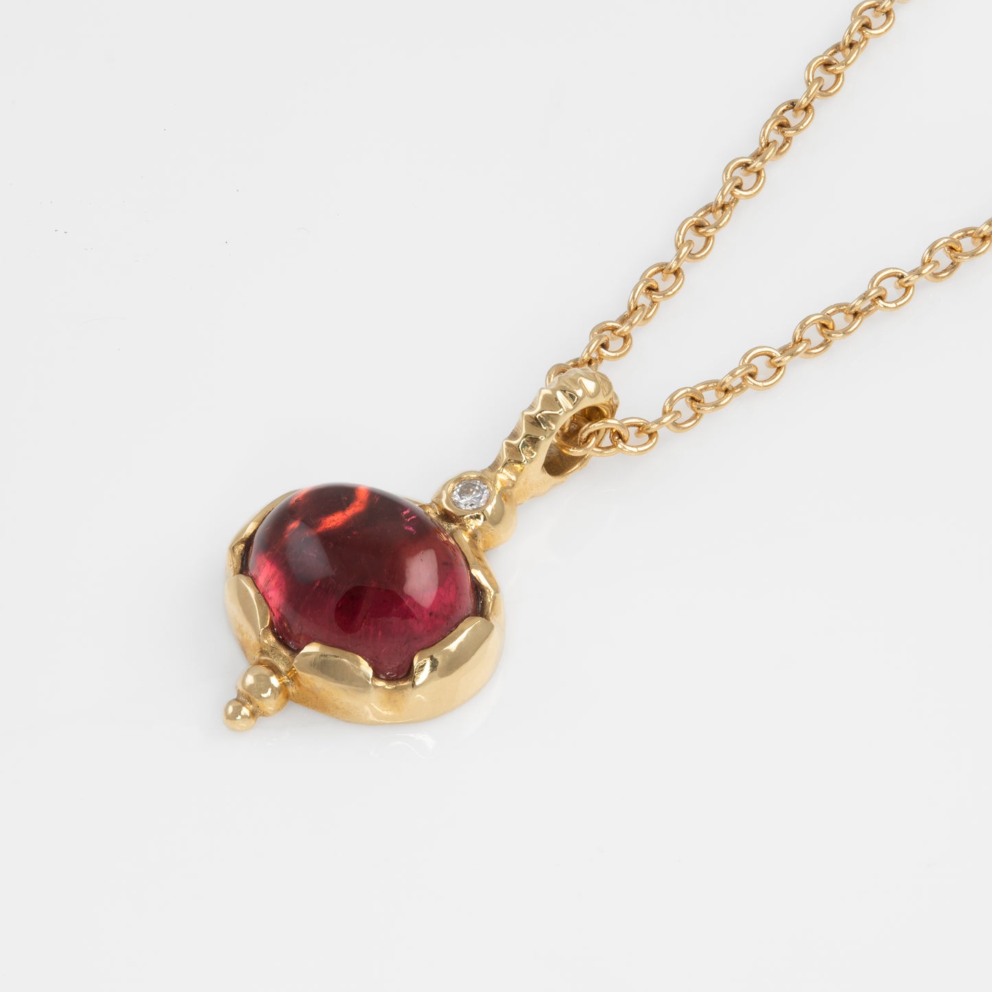 Gold necklace with a red gemstone pendant on a white background