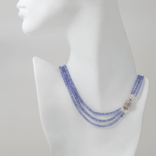 Worn on model, a three strand necklace with tanzanite and a 14 karat white gold flower clasp with milgrain finish.