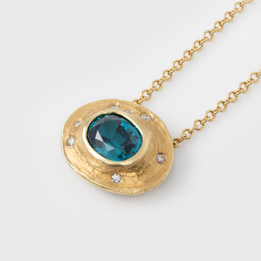 Gold necklace with a blue zircon gemstone and small accent diamonds on a white background