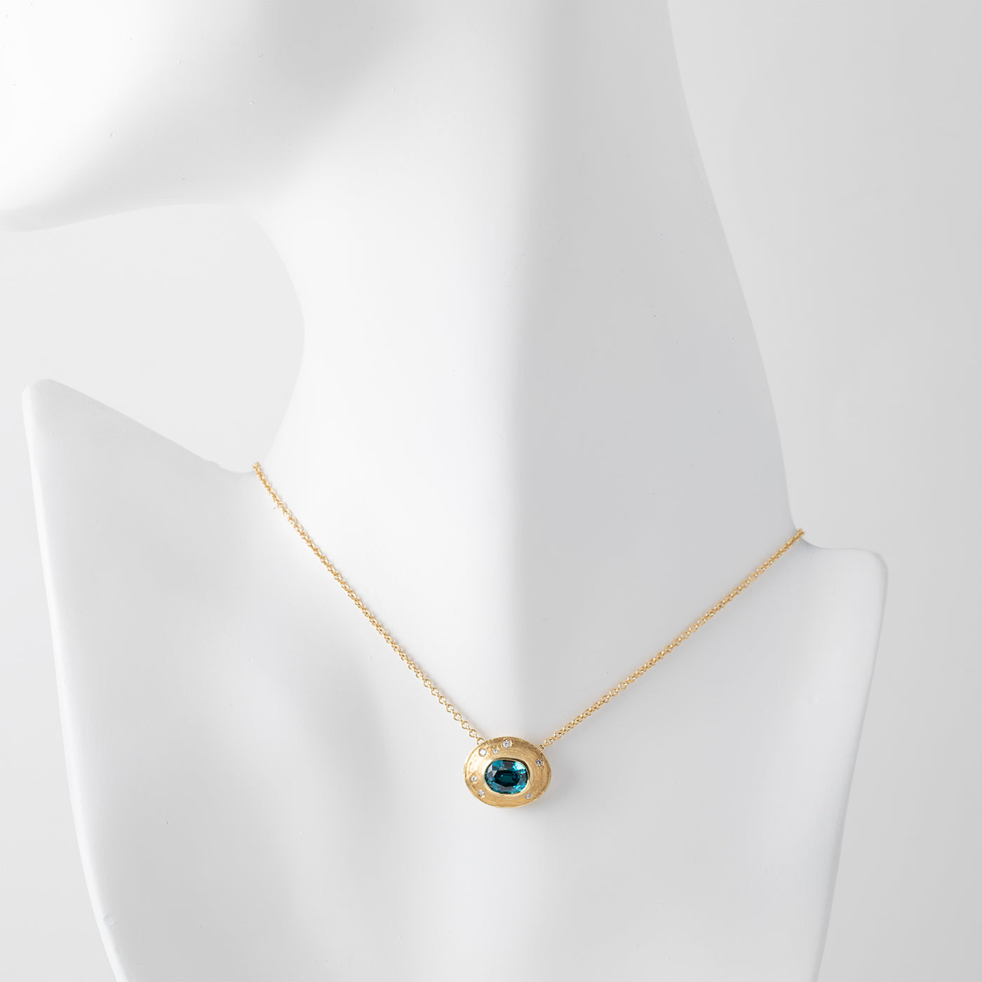 Gold necklace with a blue zircon gemstone and small accent diamonds on a white mannequin background