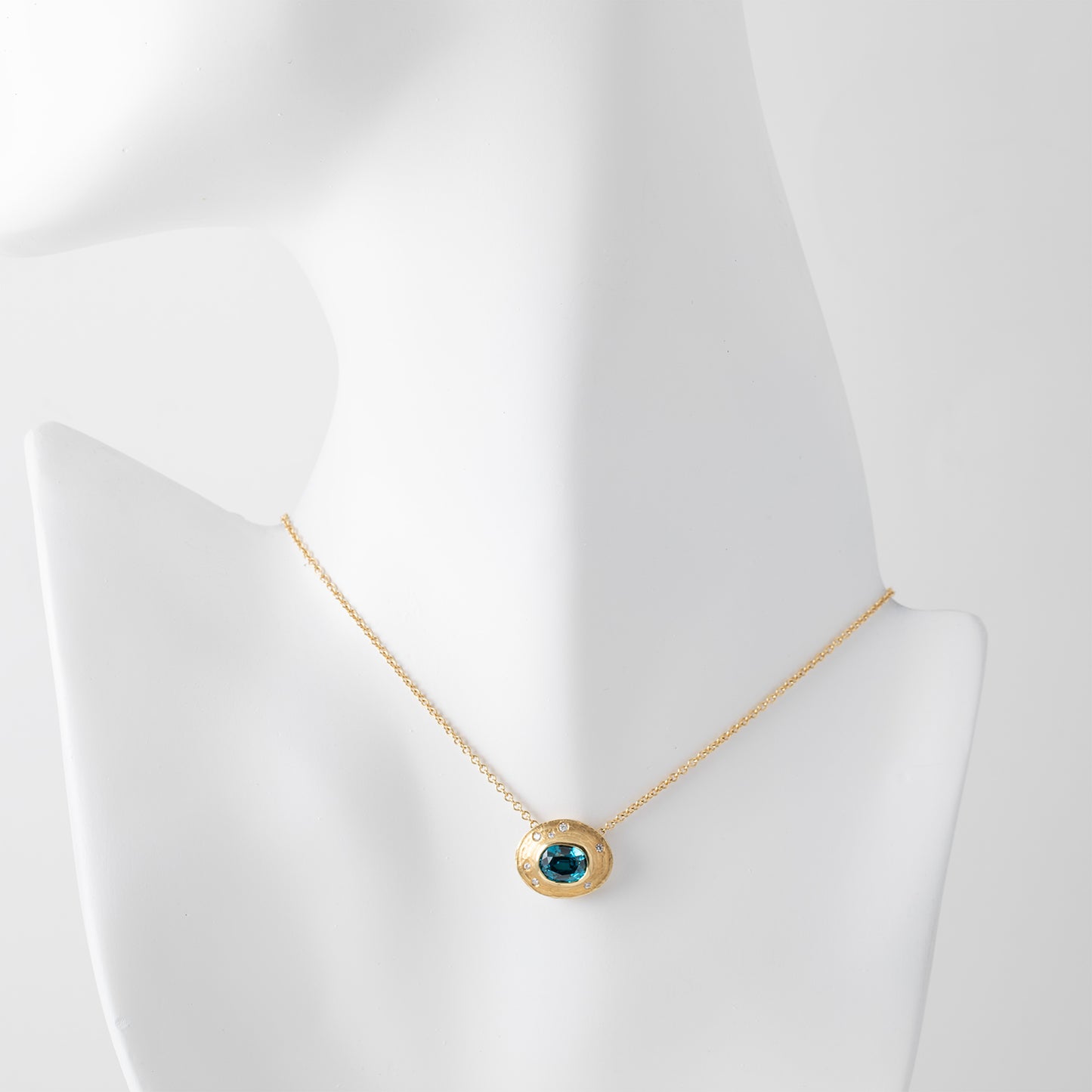 Gold necklace with a blue zircon gemstone and small accent diamonds on a white mannequin background