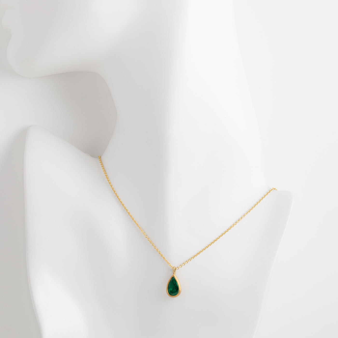 Gold necklace with a green teardrop pendant on a mannequin bust against a white background