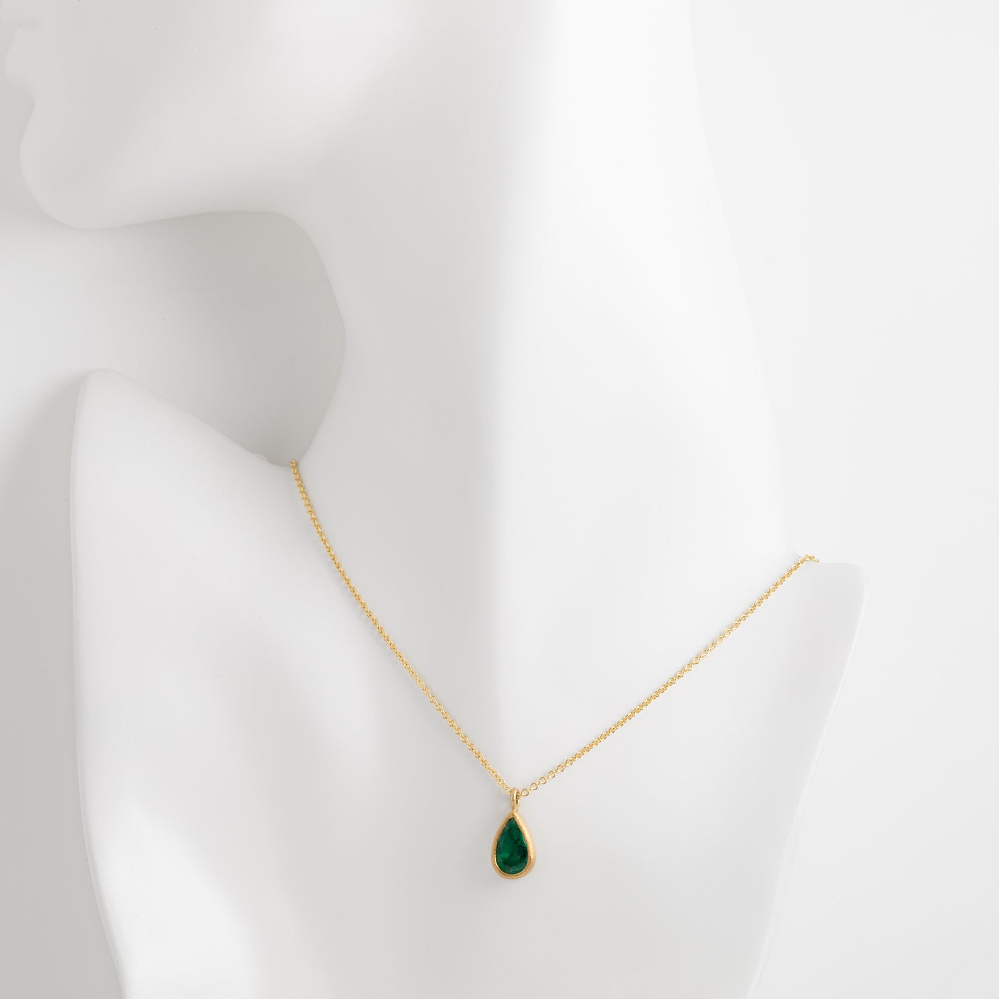 Gold necklace with a green teardrop pendant on a mannequin bust against a white background
