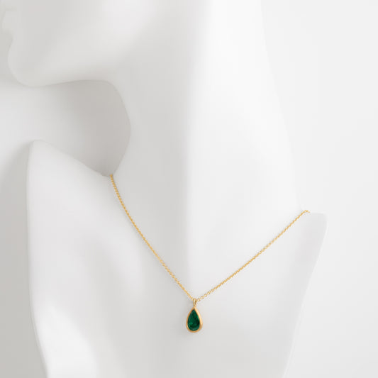 Gold necklace with a green teardrop pendant on a mannequin bust against a white background