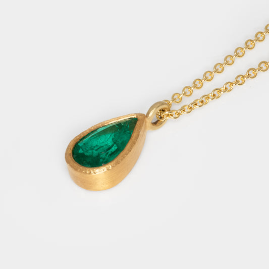 Gold necklace with a green teardrop pendant on a white background