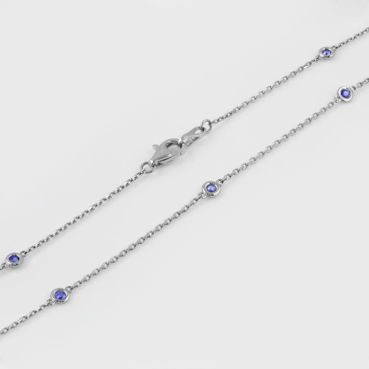 Close-up of 14k white gold station necklace featuring 10 faceted round blue Sapphires and a lobster clasp.