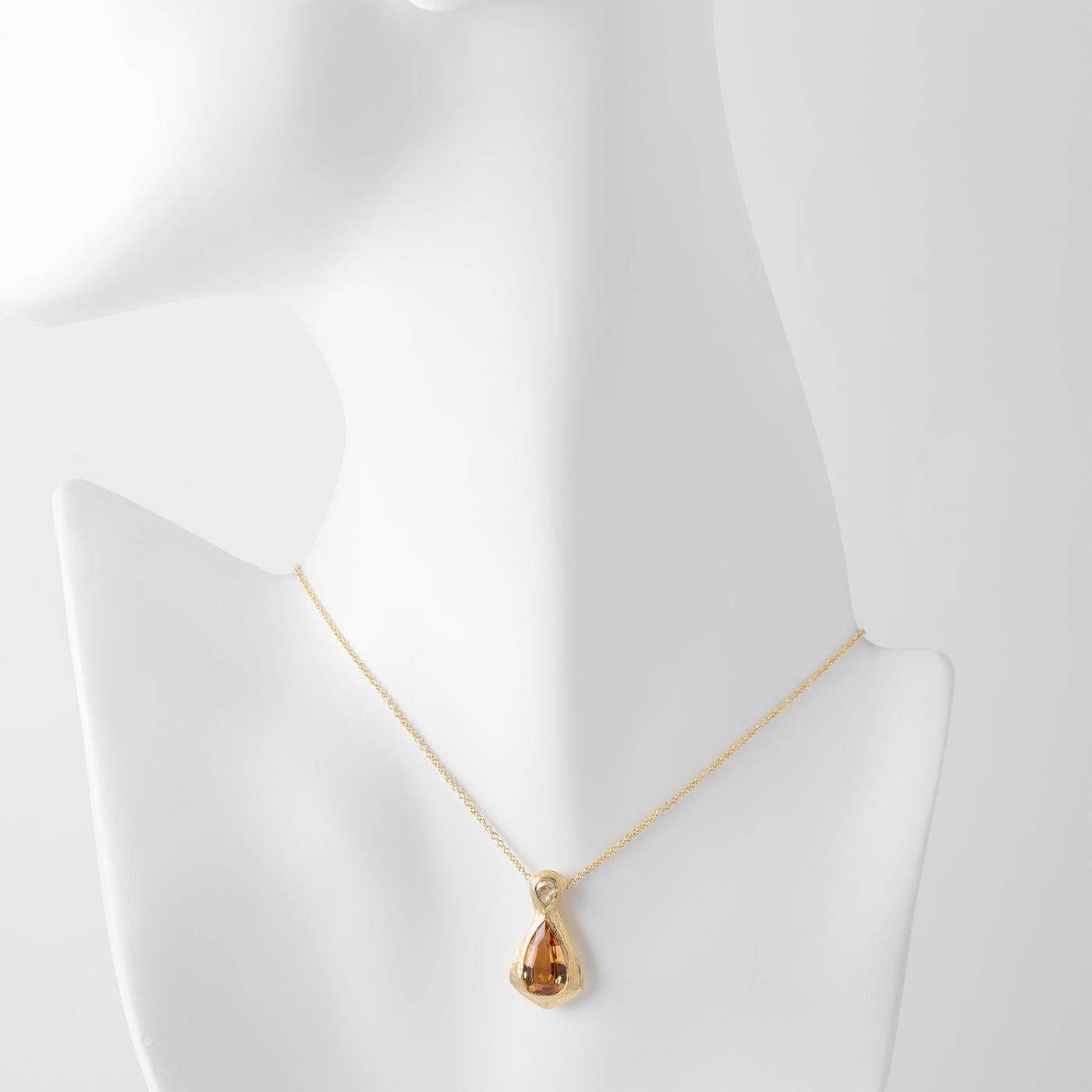 Gold necklace with a yellow orange topaz gemstone and an accent diamonds on a white mannequin background