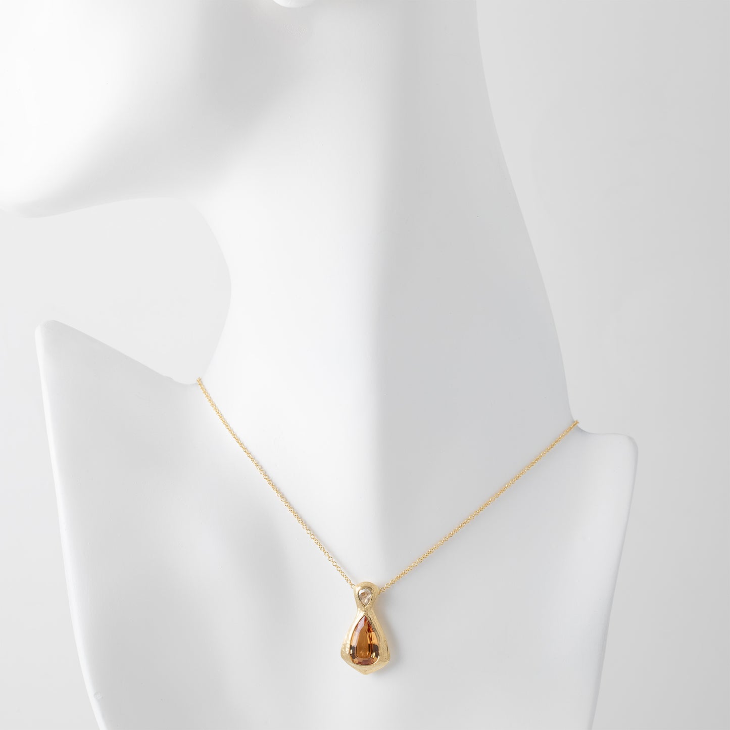 Gold necklace with a yellow orange topaz gemstone and an accent diamonds on a white mannequin background