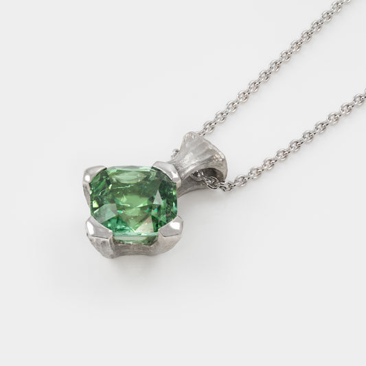 Platinum pendant with green gemstone on a white background