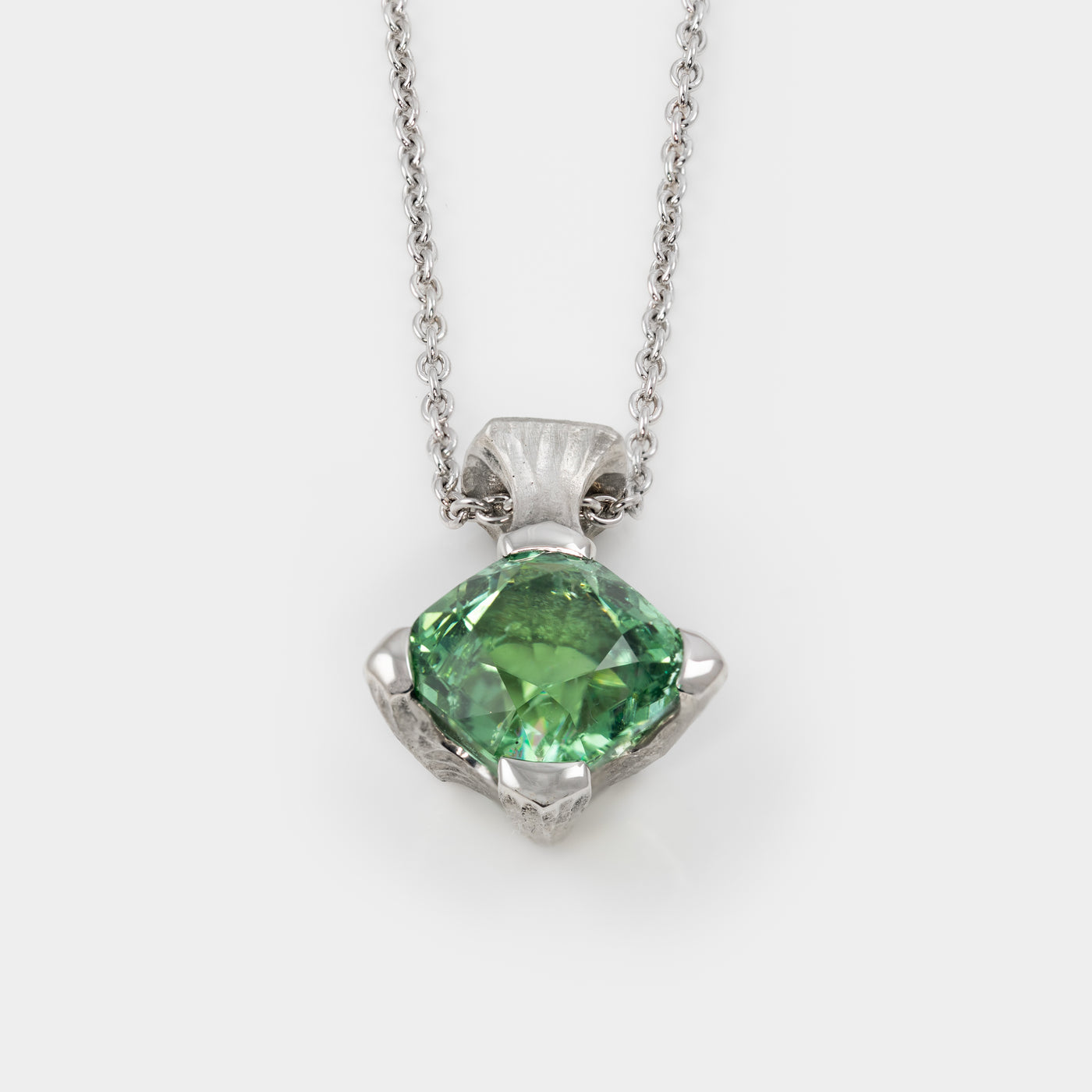 Platinum pendant with green gemstone on a white background