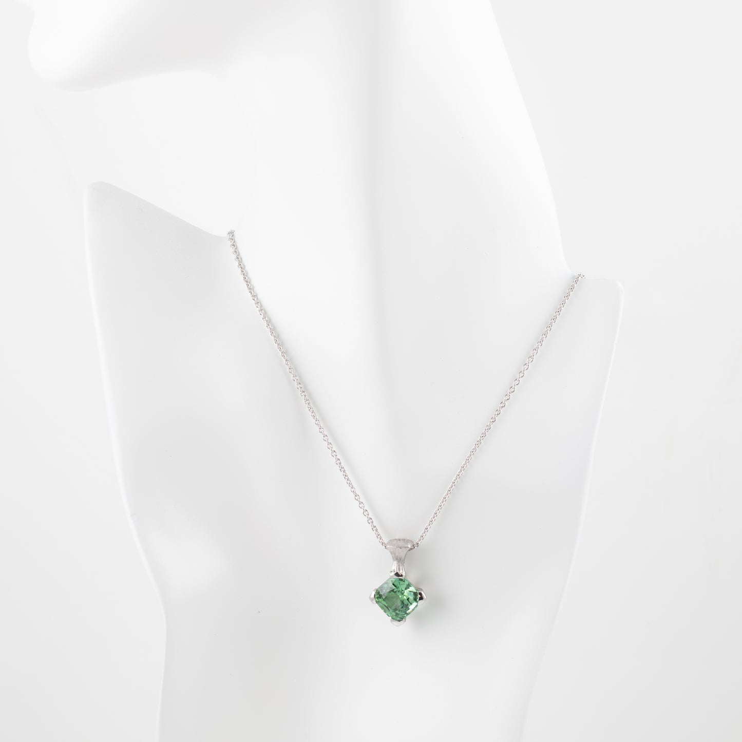 Platinum pendant with green gemstone on a white mannequin 