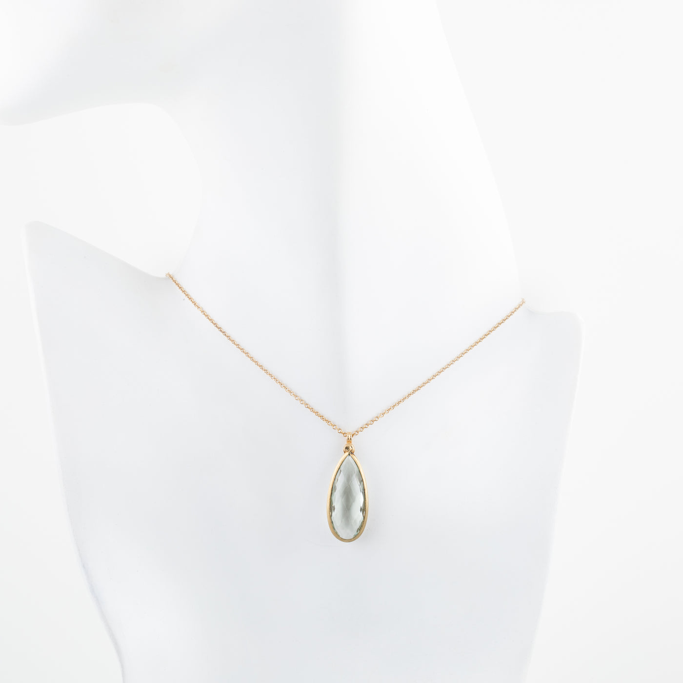 Gold necklace with a teardrop-shaped pendant on a white mannequin