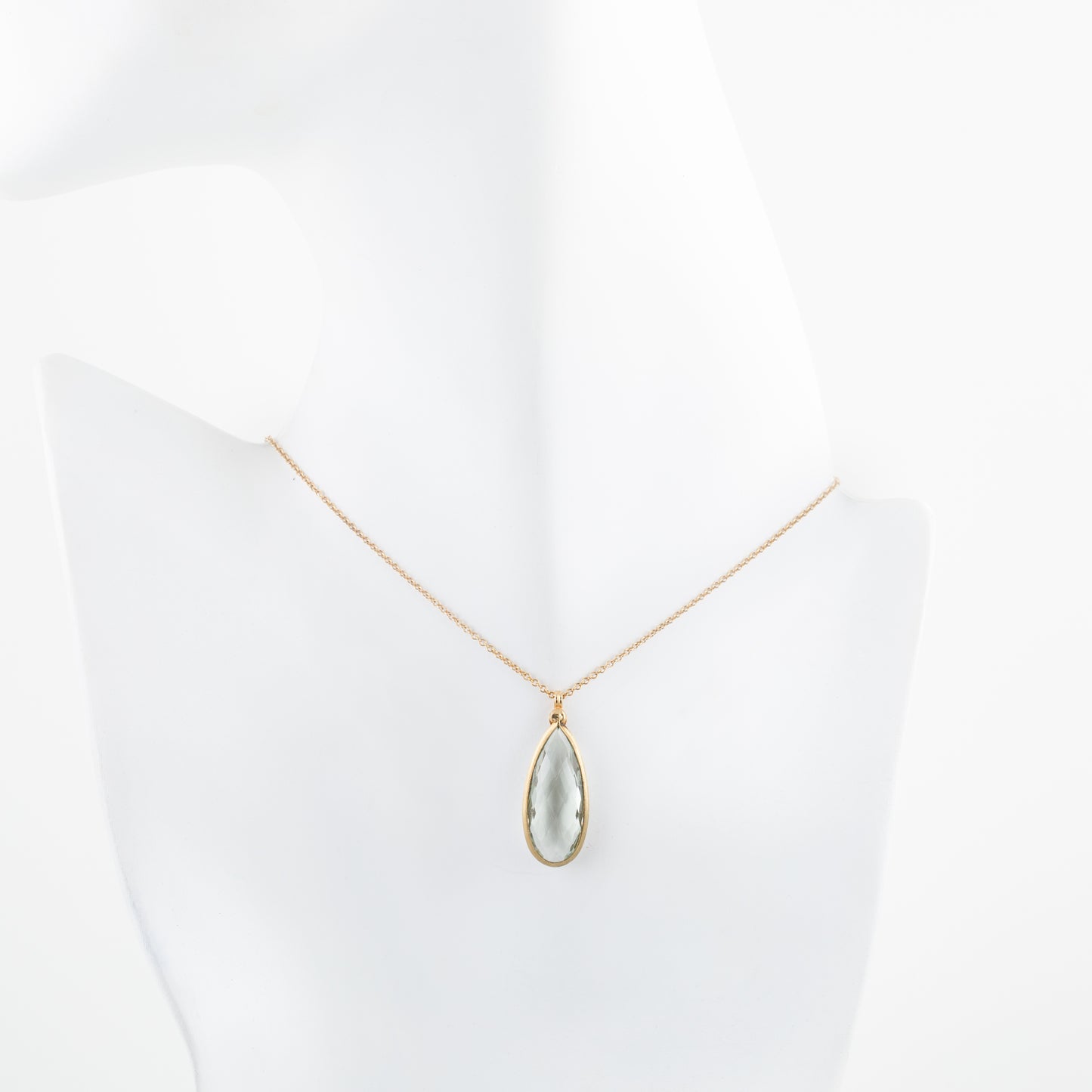 Gold necklace with a teardrop-shaped pendant on a white mannequin