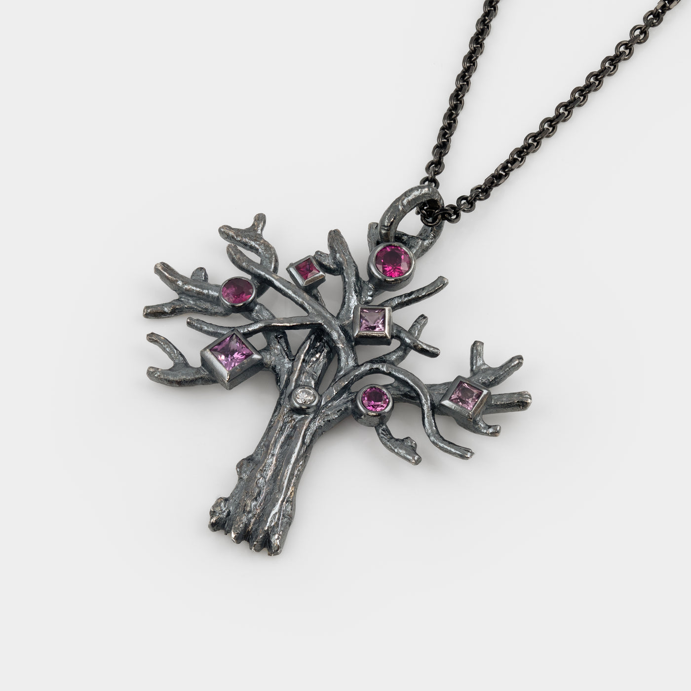 Silver tree-shaped pendant with pink gemstones on a white background