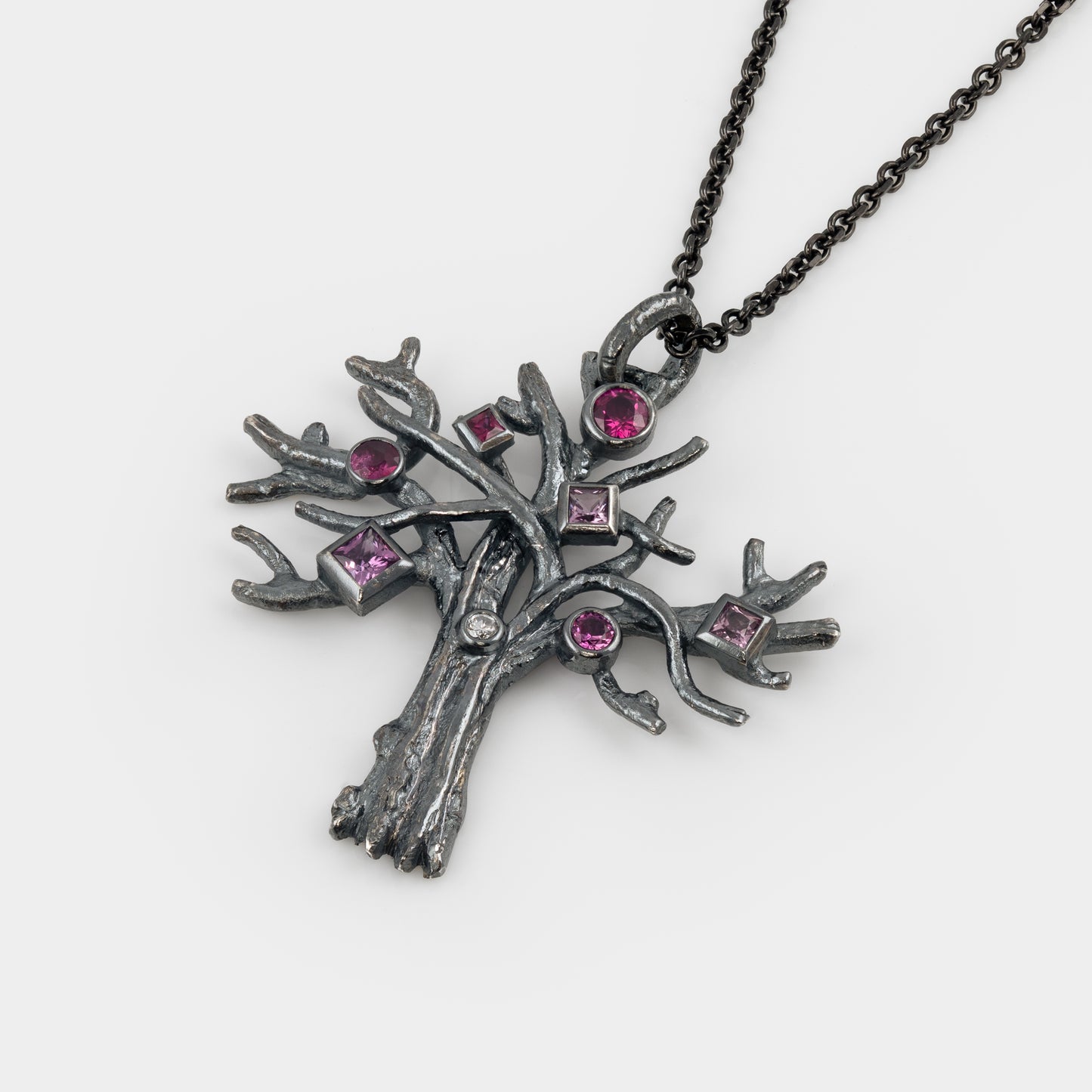 Silver tree-shaped pendant with pink gemstones on a white background