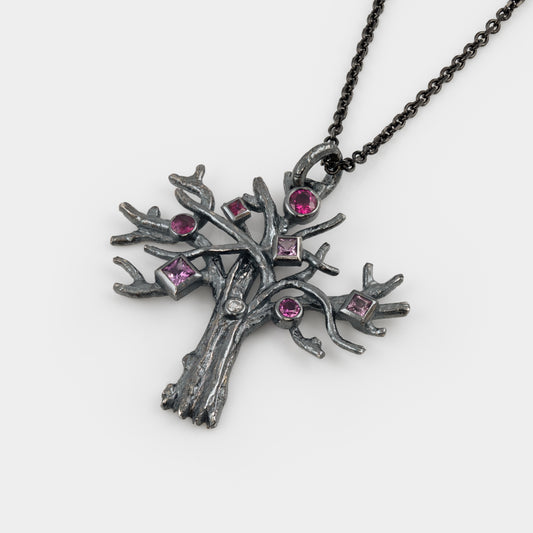 Silver tree-shaped pendant with pink gemstones on a white background