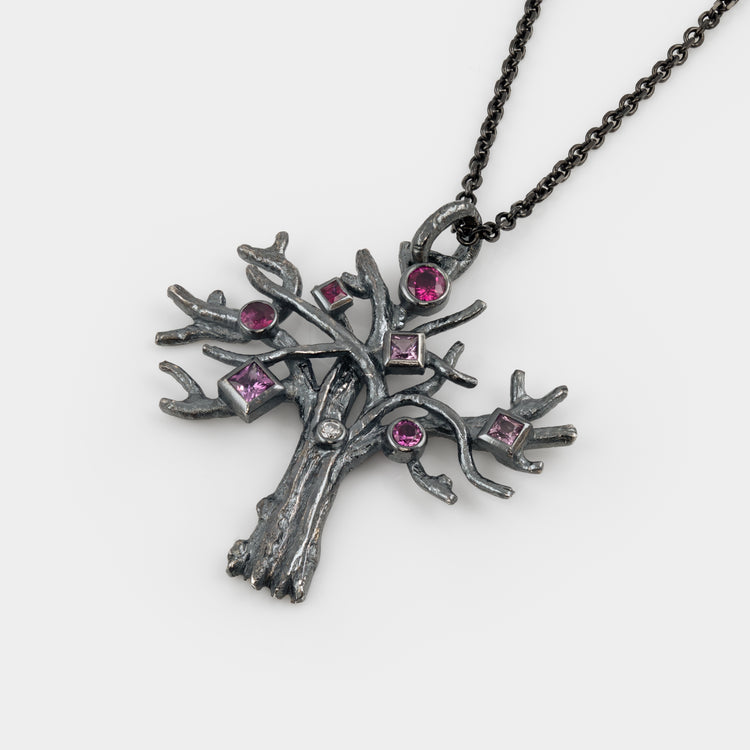Silver tree-shaped pendant with pink gemstones on a white background