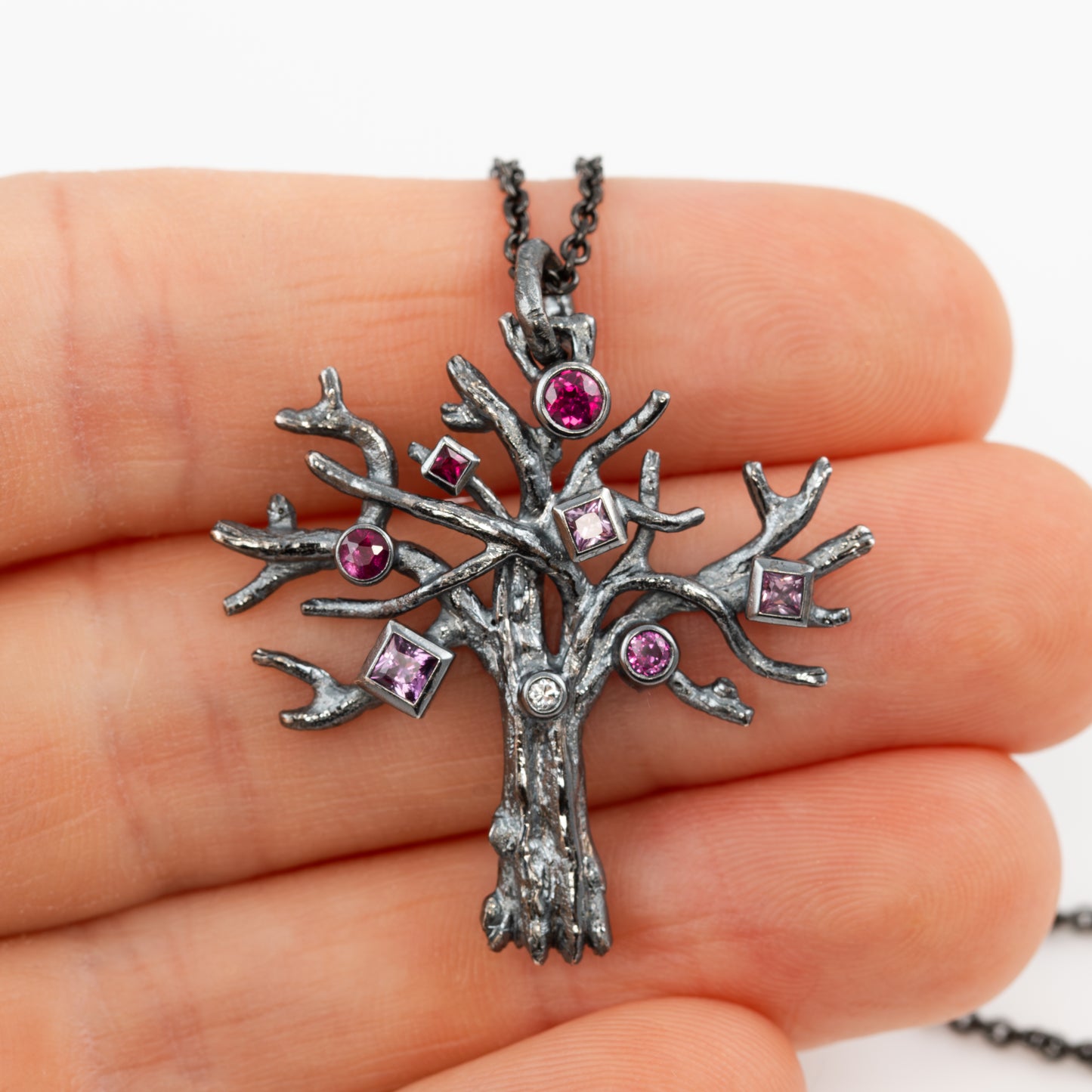 Tree-shaped pendant with embedded gemstones held in a hand against a white background