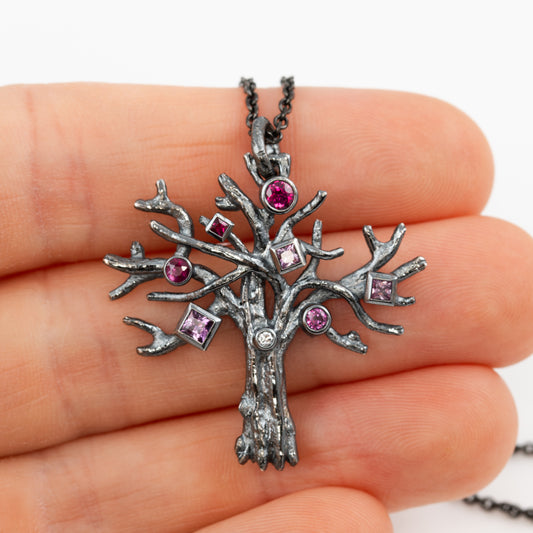Tree-shaped pendant with embedded gemstones held in a hand against a white background