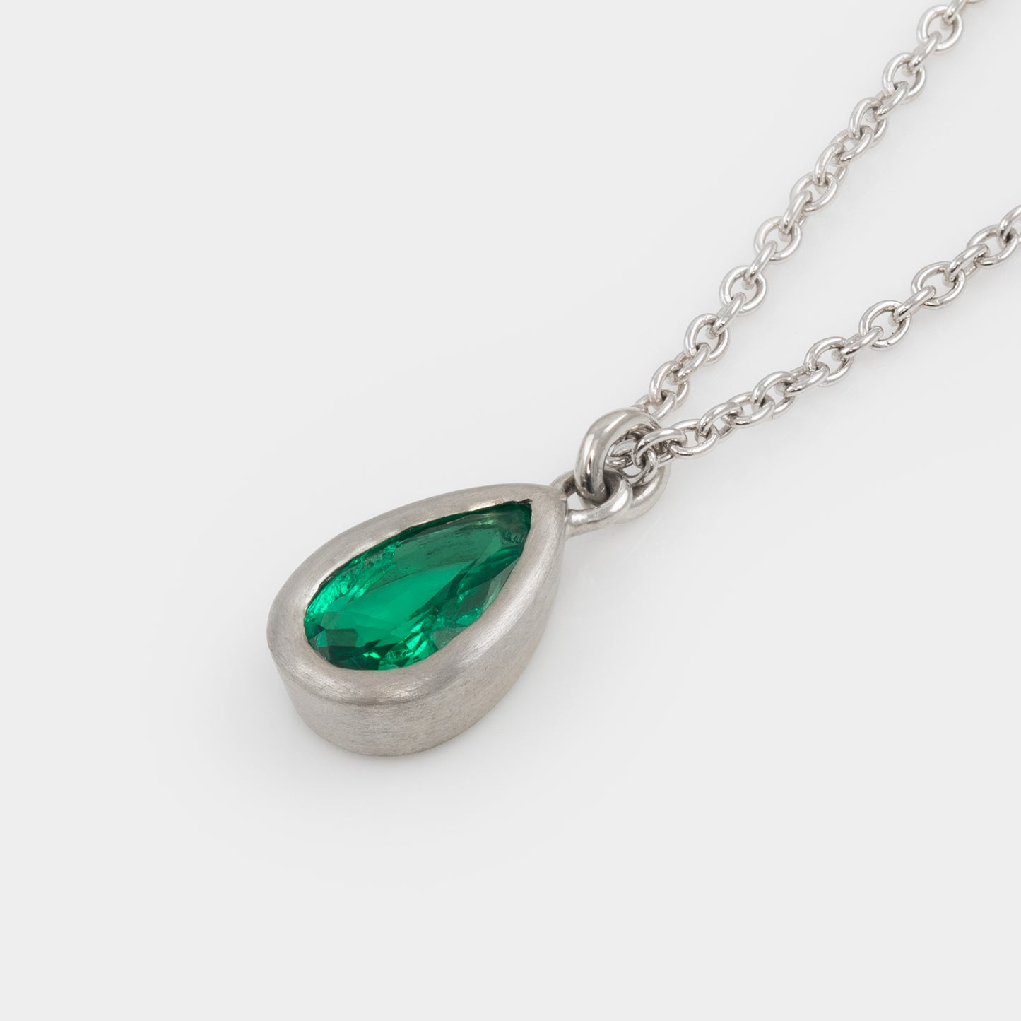 Platinum necklace with a green teardrop gem pendant on a white background