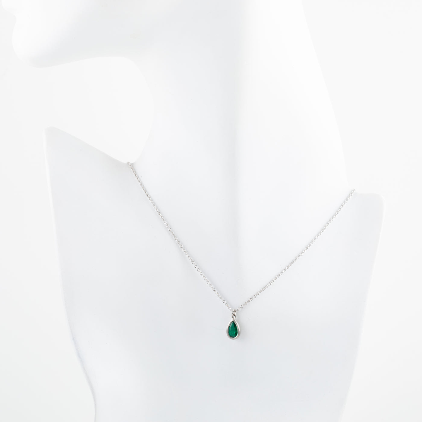 Platinum necklace with a green teardrop gem pendant on a white mannequin