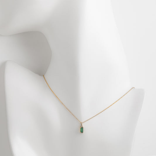Gold necklace with a green pendant on a mannequin bust against a white background