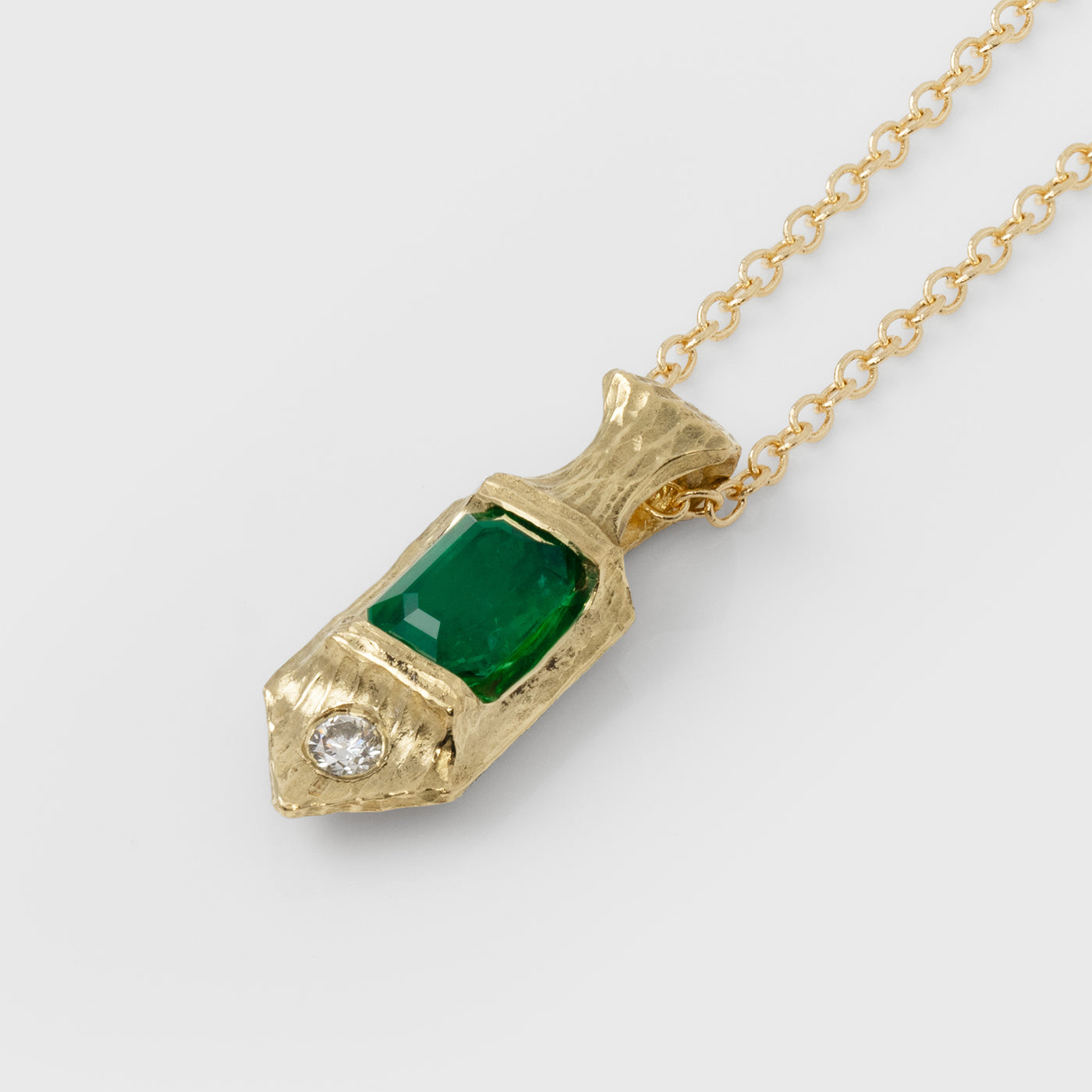 Gold necklace with a green emerald gemstone pendant on a white background