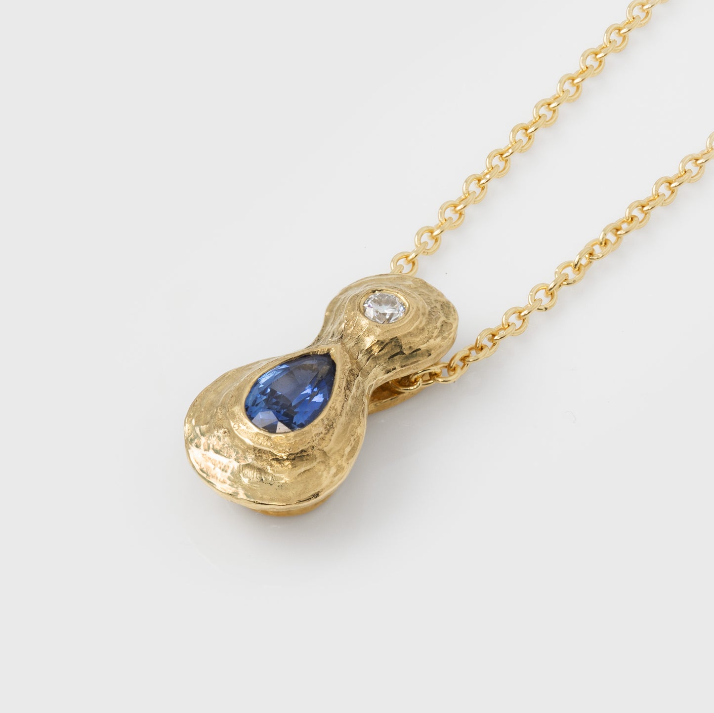 Gold pendant with a blue sapphire gemstone and an accent diamond on a white background