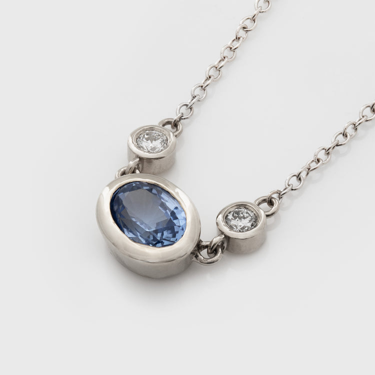 Gold necklace with a blue sapphire gemstone and small accent diamonds on a white background