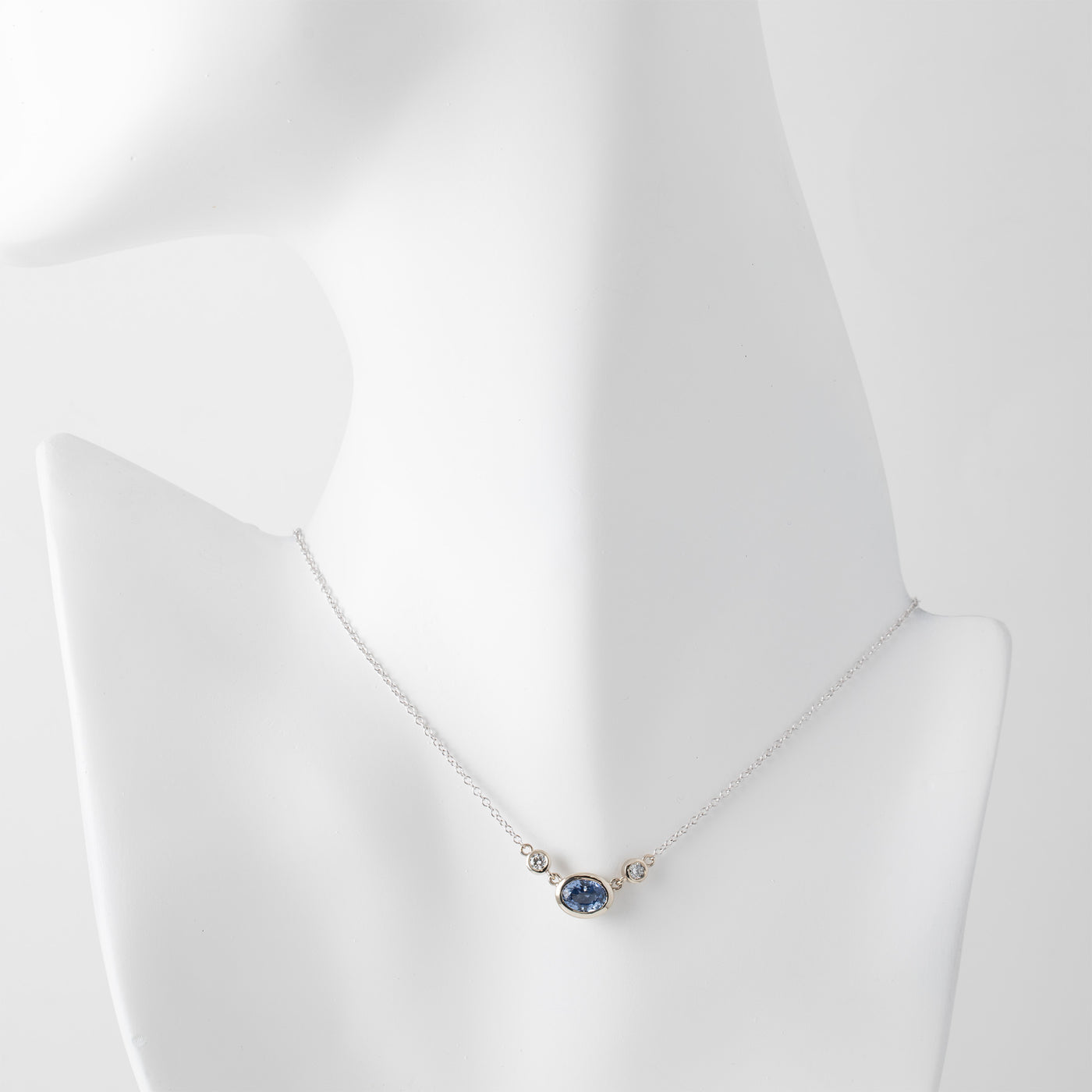 Gold necklace with a blue sapphire gemstone and small accent diamonds on a white mannequin background