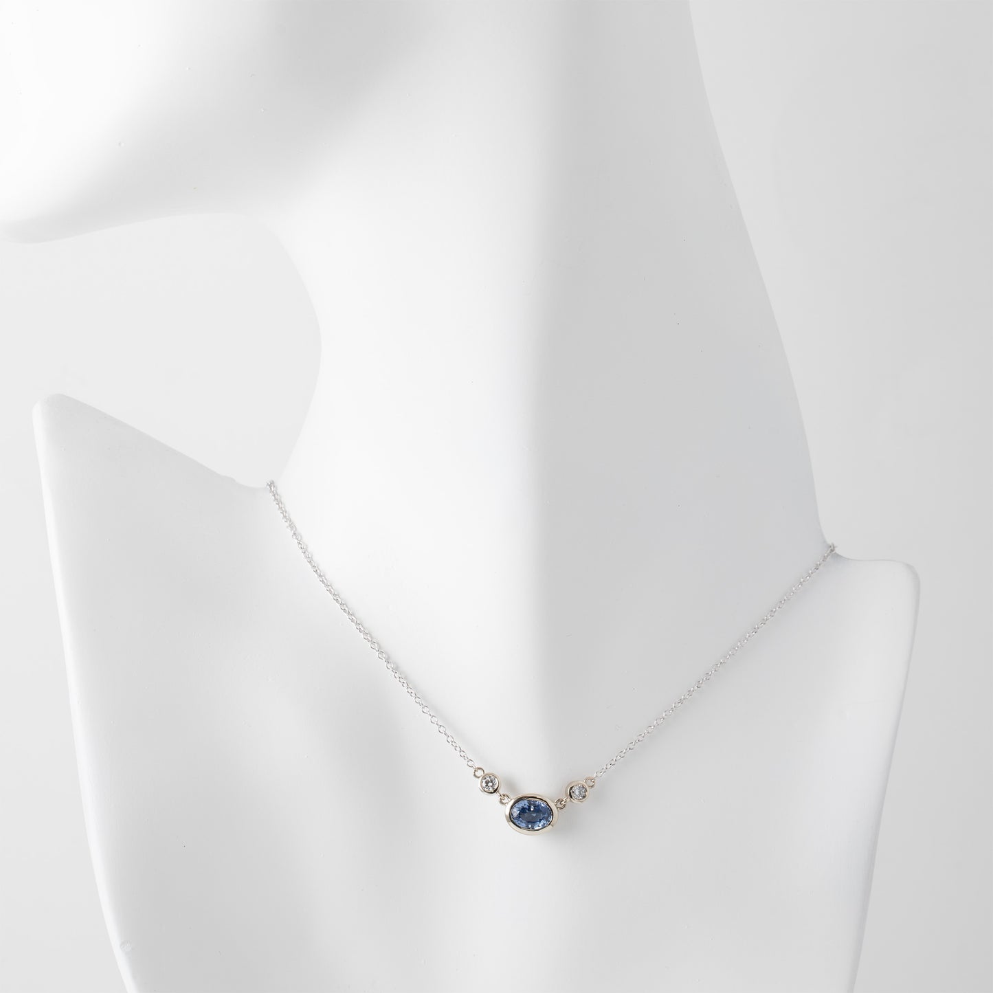 Gold necklace with a blue sapphire gemstone and small accent diamonds on a white mannequin background
