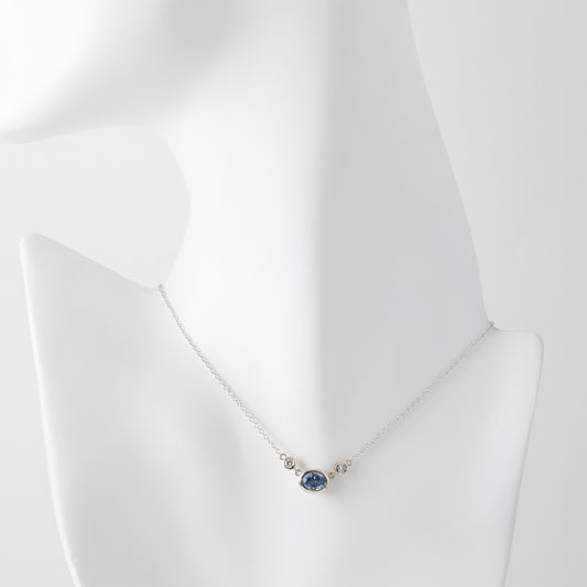 Gold necklace with a blue sapphire gemstone and small accent diamonds on a white mannequin background