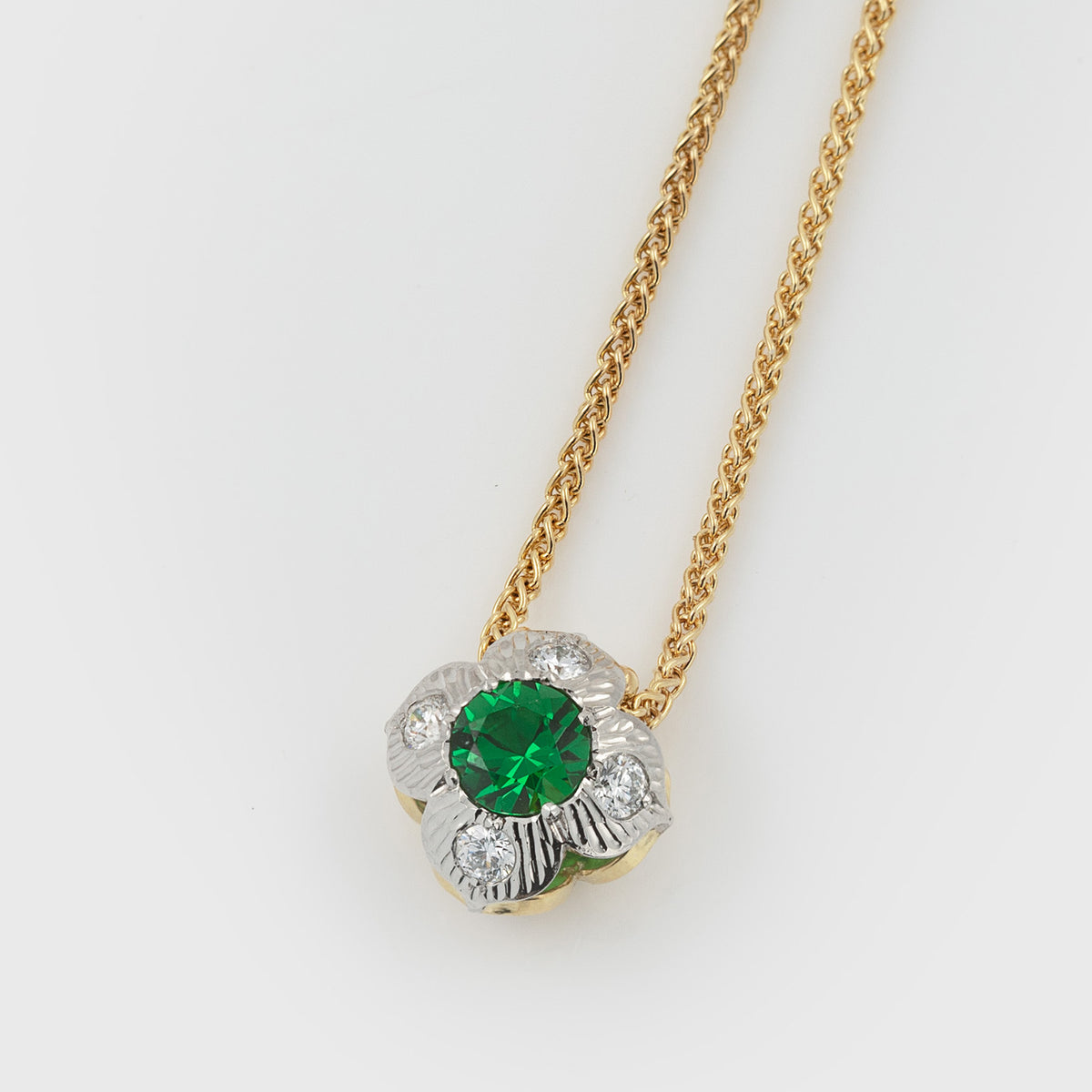 Double-sided flower pendant featuring green gemstone and diamonds, suspended from a yellow gold chain, photographed on a white background.