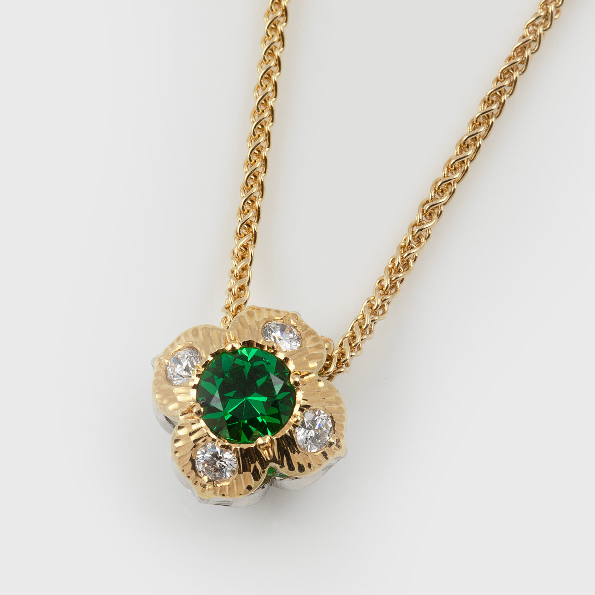 Double-sided flower pendant featuring green gemstone and diamonds, suspended from a yellow gold chain, photographed on a white background.