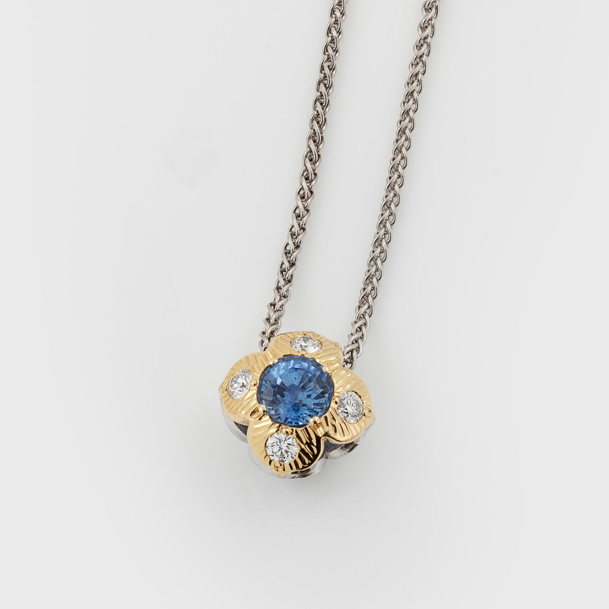Flower pendant featuring blue sapphires and diamonds, suspended from a platinum chain, photographed on a white background.