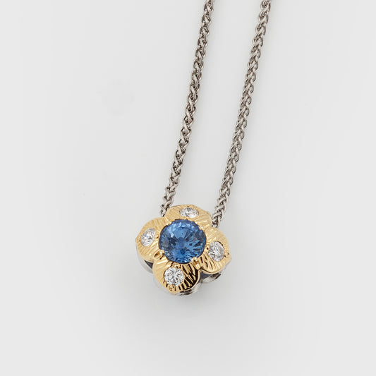 Flower pendant featuring blue sapphires and diamonds, suspended from a platinum chain, photographed on a white background.