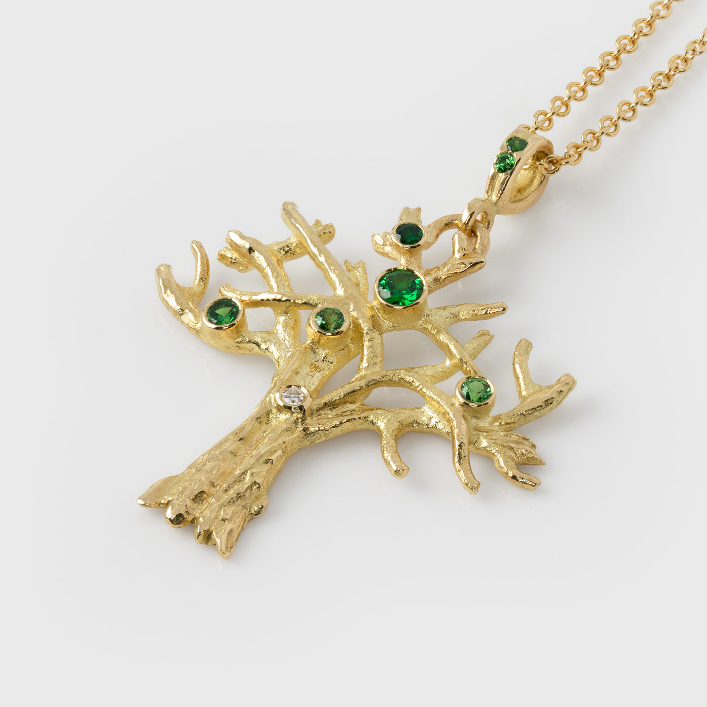 Gold tree-shaped pendant with green gemstones on a white background