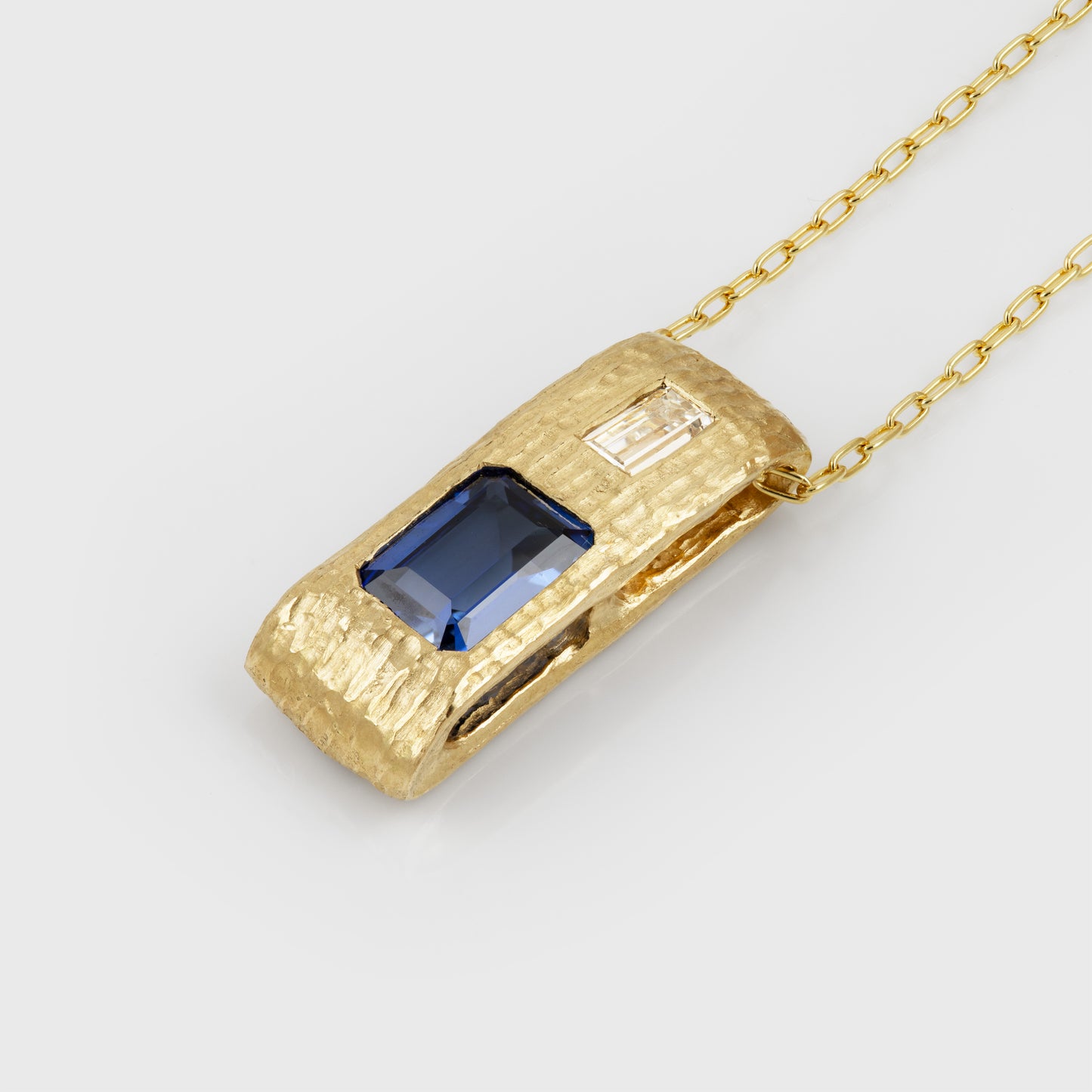 Angled view of yellow gold pendant feauturing emerald cut blue Sapphire and baguette cut Diamond