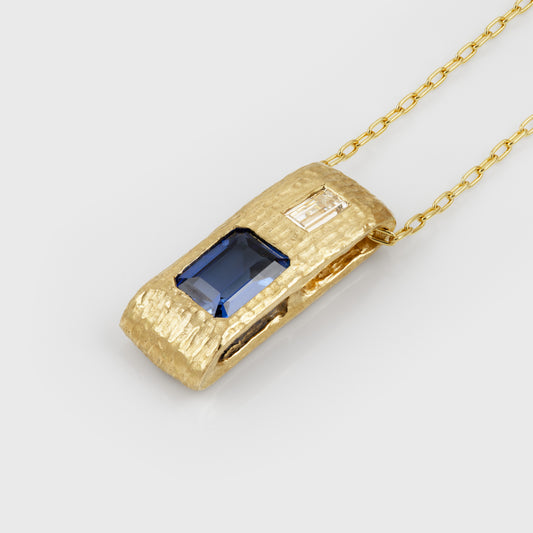 Angled view of yellow gold pendant feauturing emerald cut blue Sapphire and baguette cut Diamond