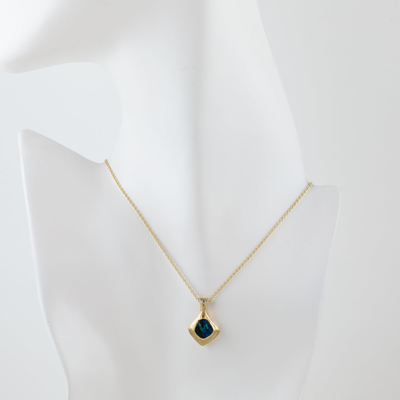 Gold natural texture necklace with a blue and green opal gemstone and accent diamond on a white mannequin