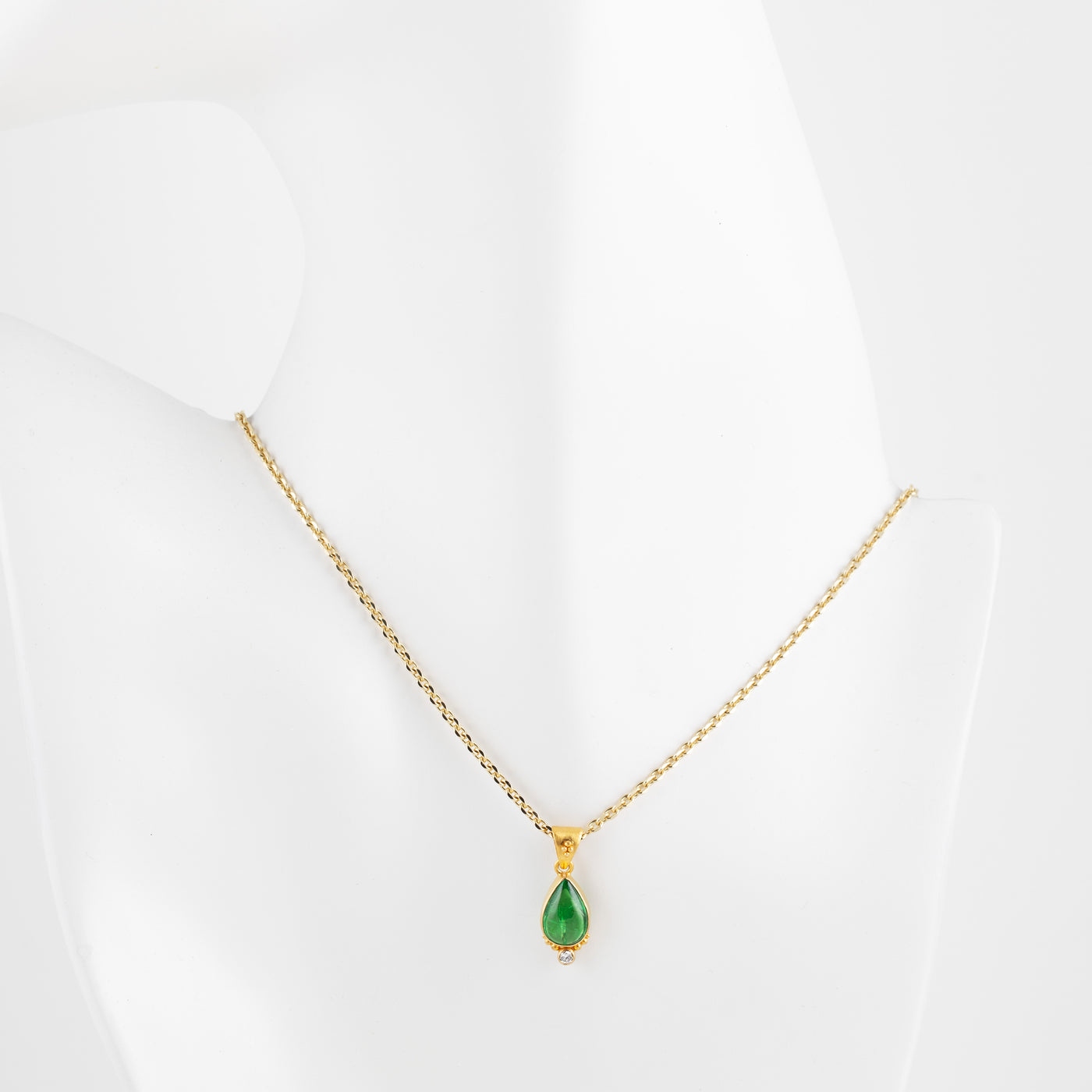 Gold necklace with a green gemstone on a white mannequin