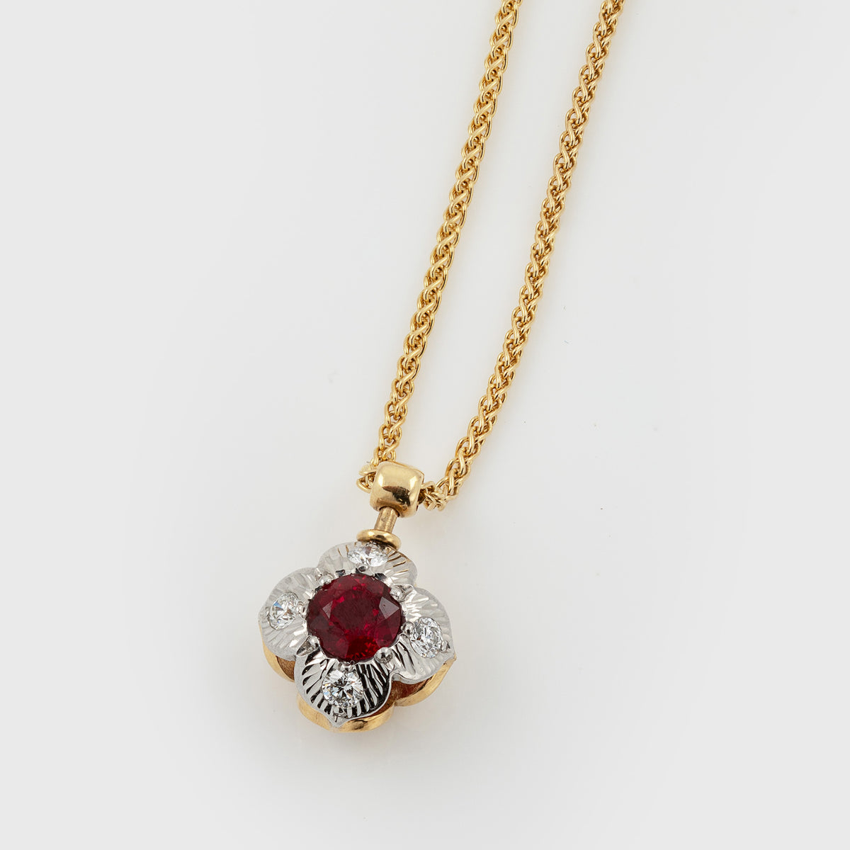 Two-tone flower pendant featuring faceted round red gem and diamonds, suspended from a yellow gold wheat chain, photographed on a white background.
