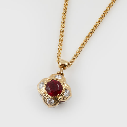 A gold chain necklace with a flower-shaped pendant featuring a central round ruby gemstone and four smaller diamonds set in gold frame, photographed on a light gray background.