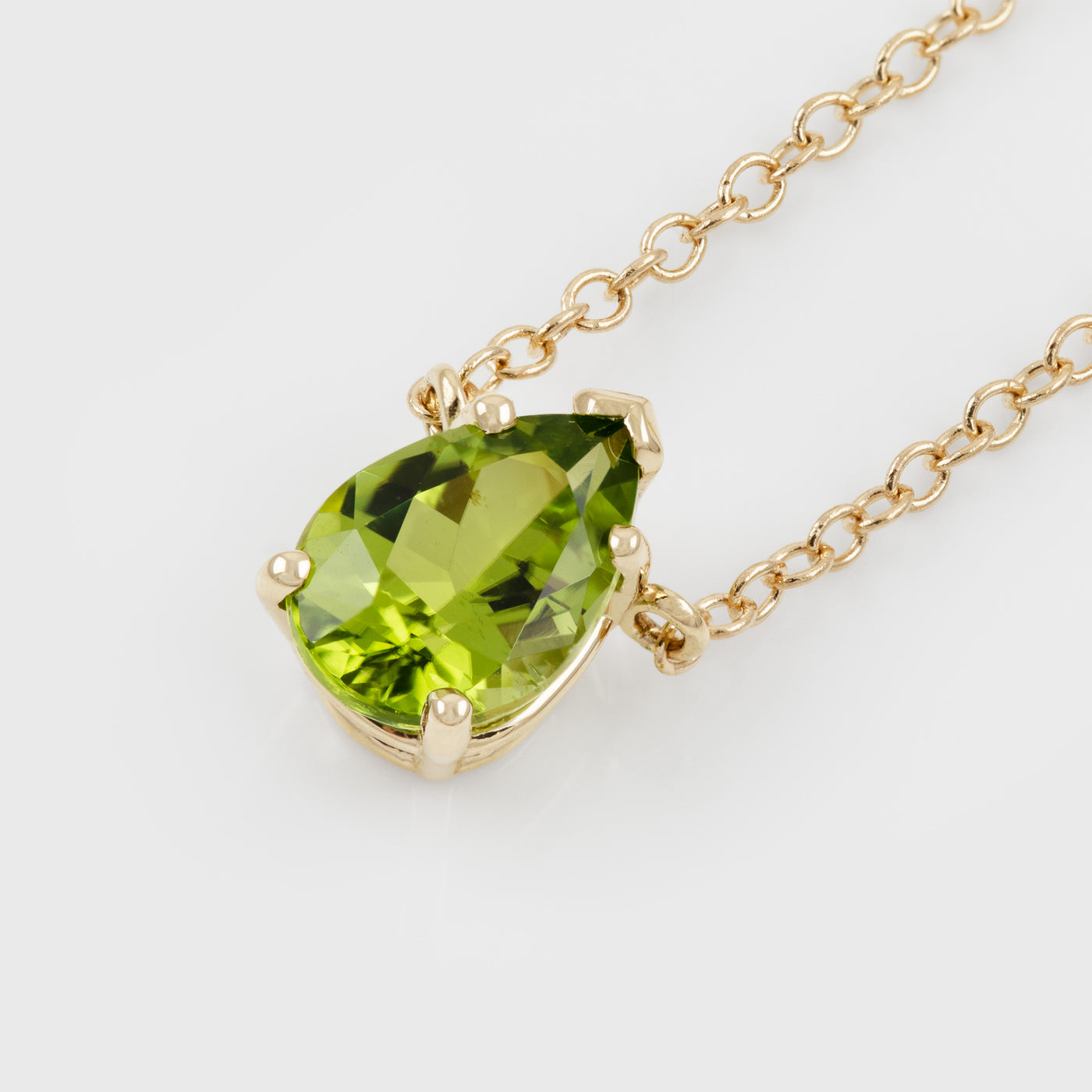 A gold pendant necklace featuring a green peridot gemstone in a four-prong setting, suspended from a delicate gold chain against a clean white background.