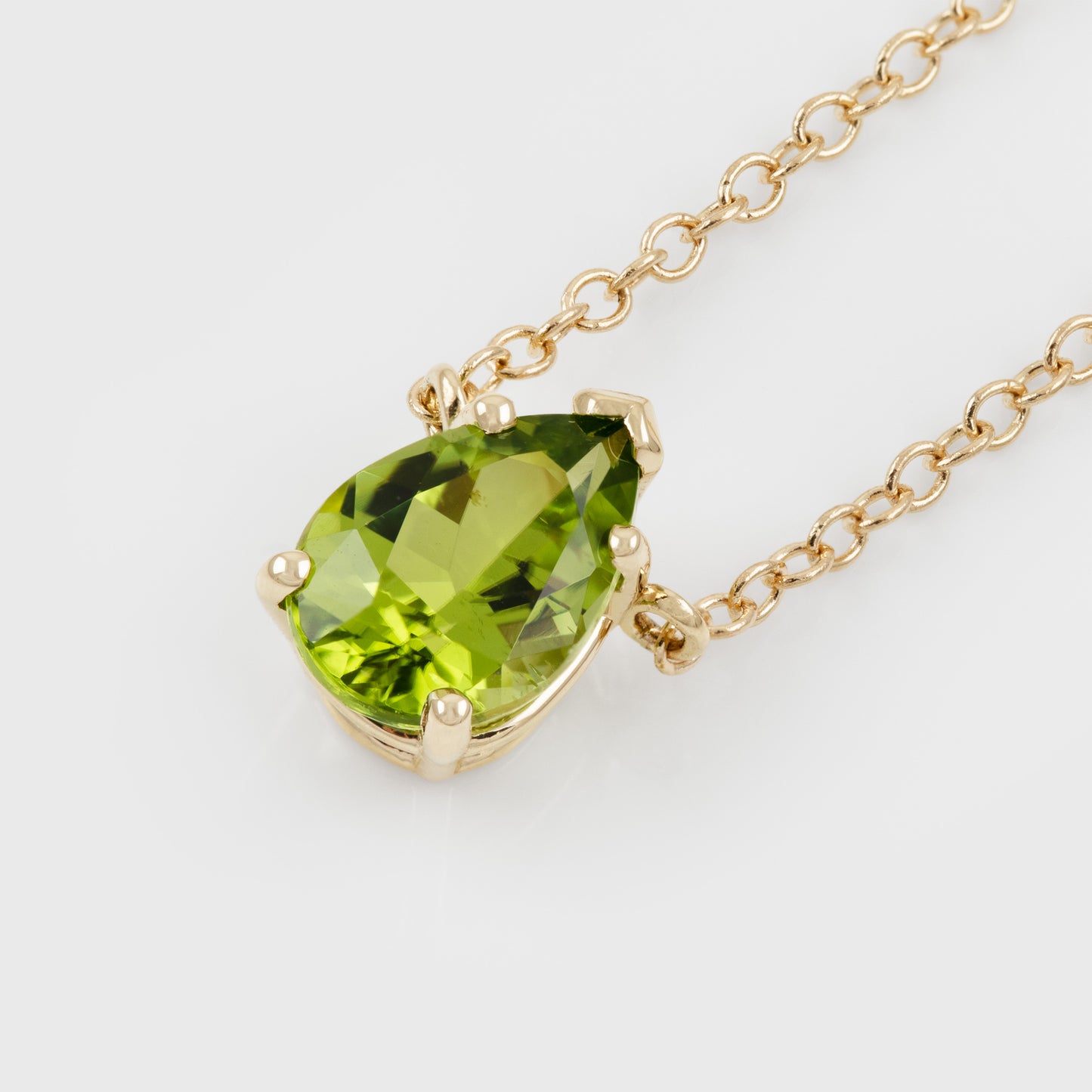 A gold pendant necklace featuring a green peridot gemstone in a four-prong setting, suspended from a delicate gold chain against a clean white background.