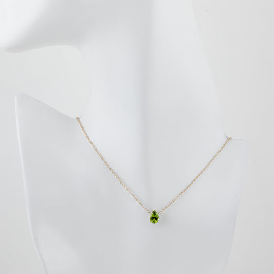 A delicate gold chain necklace with a green teardrop-shaped peridot gemstone pendant, displayed on a white mannequin bust against a clean white background.