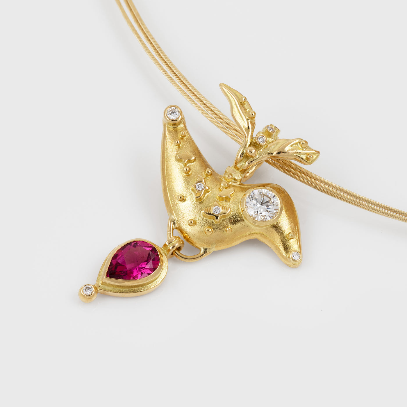 A gold bird pendant charm with a teardrop-shaped pink gemstone and diamonds, shown on a gold necklace against a light gray background.