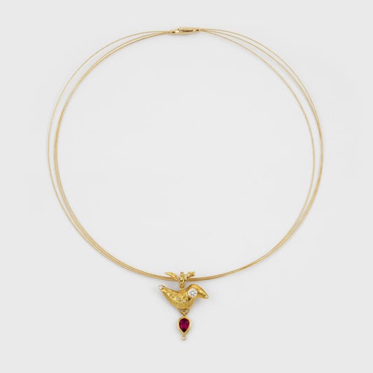A delicate triple-strand gold necklace featuring a small bird-shaped pendant with a diamond and a dangling red teardrop gemstone, set against a plain light gray background.
